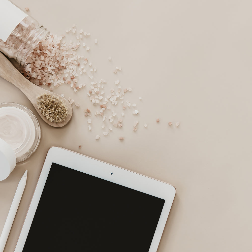 Face cream, bath salts and a tablet on a beige table